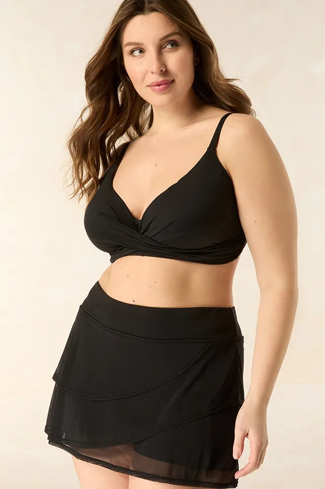 Coco Reef - woman on beige background in black bikini top and swim skirt